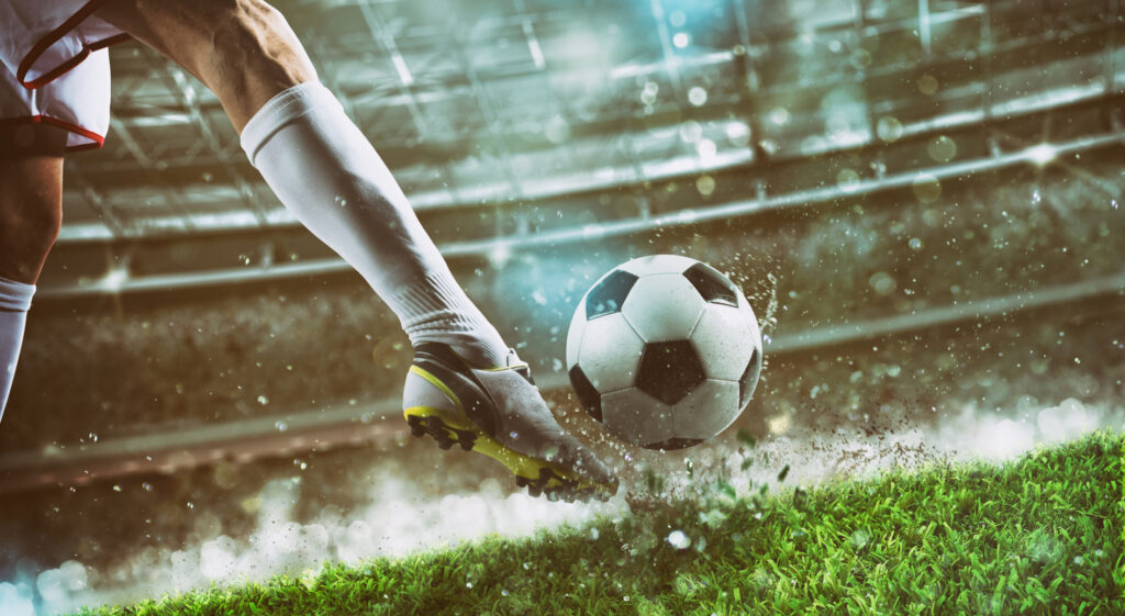 Gamba di un calciatore mentre calcia un pallone su un campo da calcio